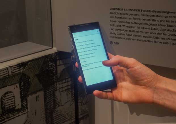 Media-Guide mit einem Lesetext in leichter Sprache vor einem Objekt aus der Dauerausstellung