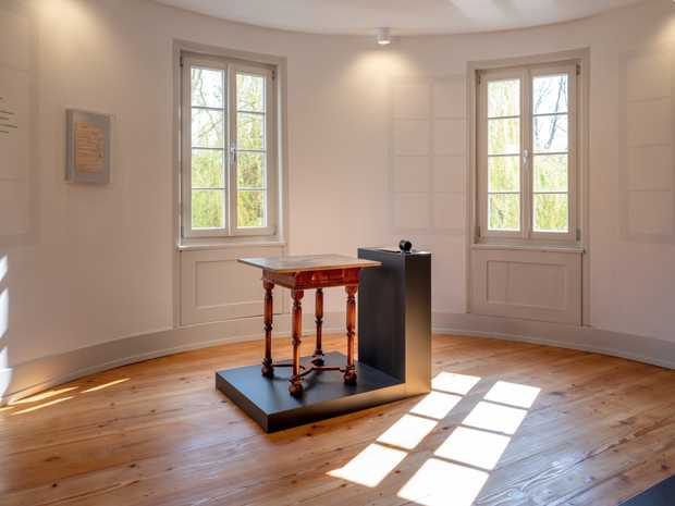 Ein heller Raum mit einem alten Holzboden und einem kleinen Schreibtisch in der Mitte.