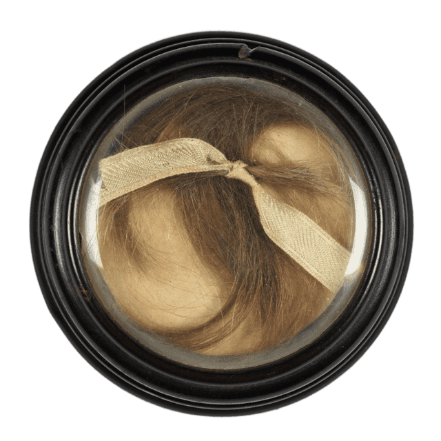 Ein rundes Medaillon mit schwarzem Rand. Darin liegt eine dunkelbraune Haarsträhne mit einer weißen Schleife.