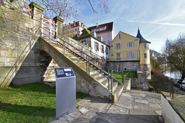 Eine große Steintreppe mit einem Holztor führt in einen Garten. Am Garten fließt der Neckar vorbei.