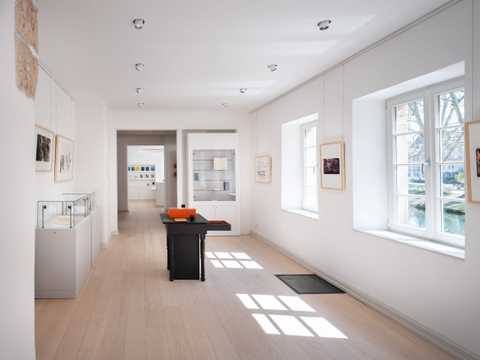 Bild des zweiten Raumes der Dauerausstellung: Mehrere weiße Vitrinen an den Wänden, in der Mitte eine Medienstation zur Wirkung Hölderlins in der Musik, der Literatur und den Künsten